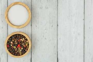 Salt and pepper seasoning in wooden bowls stands on the left on a white wooden background with space for text. The concept of seasonings, spices, flavorings. High quality photo 