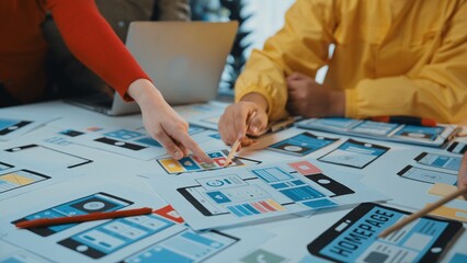 Obraz premium Close-up of a collaborative workspace featuring hands selecting user interface mockups from a table. Laptops and digital tools create an engaging environment for creative professionals. SACTR