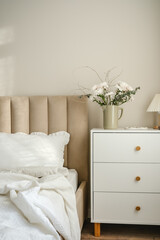 A serene bedroom with a stylish bed, plush pillows, and fresh flowers on white dresser artfully arranged in the room.