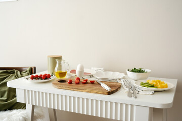 A beautifully arranged dining table with cutting board, fresh, vibrant ingredients - tomatoes, ham, aragula, fruits, olive oil, ready for cooking and meal preparation.
