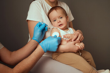 A healthcare professional administers a vaccine to a toddler sitting on a caregiver's lap. The...