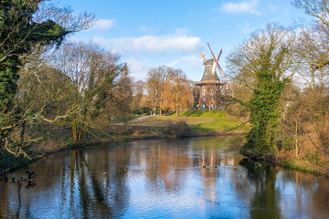 An idyllic pond surrounded by trees and a traditional windmill on a gentle hill