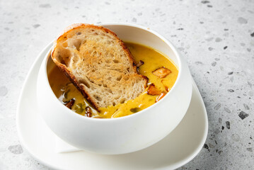 A warm bowl of creamy soup garnished with crispy bread, set on a textured surface. Ideal for food photography, showcasing comfort and deliciousness.