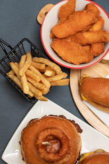 Buffet table scene of take out or delivery foods. French fries, hamburgers, fried chicken, wraps and sides. Above view on a dark background