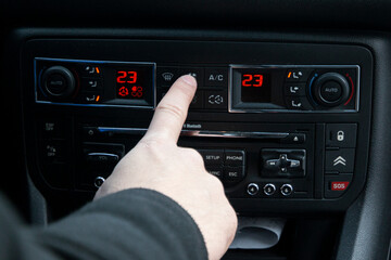 Hand pointing at dual-zone climate control on a car dashboard, showcasing advanced automotive features and comfort.