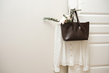 A chic white blouse elegantly draped over a door, paired with a dark brown handbag and decorative...
