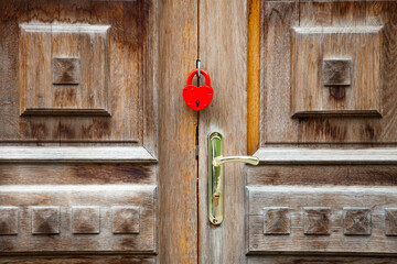 The old wooden panel door with a gold-colored lever handle is locked with a red padlock. This door blocks the entrance for visitors to the emergency zone