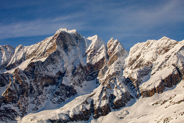 The mountain landscape has snow-covered slopes under the blue sky. The summits of these mountains look like a hacksaw, creating a dangerous path for alpinists who want to traverse these peaks.