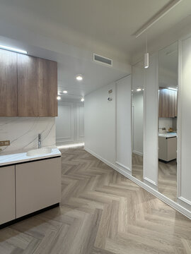 A contemporary apartment interior showcases a spacious layout with sleek wooden flooring and modern lighting fixtures. The kitchen area features minimalist cabinetry for a clean look.