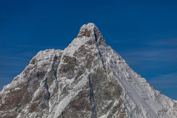 A snow-covered Matterhorn mountain against the blue sky. On the mountain slope, you can see a small hut for alpinists caught in a storm. This building is called Solvay