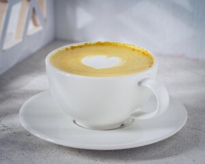 A warm and creamy turmeric latte with a heart-shaped latte art design, served in a white ceramic...