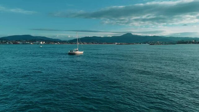 Voilier navigue sur un oc&eacute;an calme en bordure de c&ocirc;te basque et sa vue sur montagnes d'Ascain 