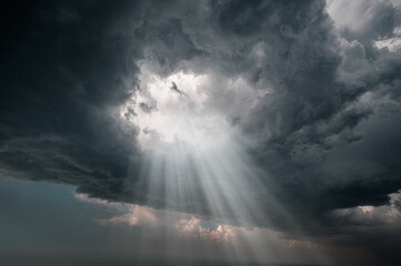 Rays of light through the hole in the dark stormy clouds in the sky.