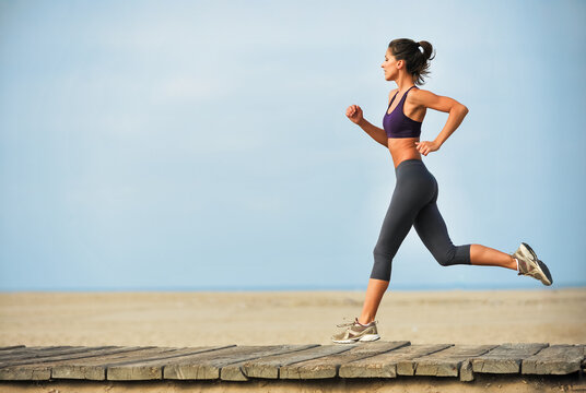 Pretty young Caucasian woman running along boardwalk on Santa Monica Beach wearing leggings and sports bra.