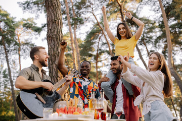 Multicultural group of people, bearded hipster man playing guitar and friends dancing, singing and having fun