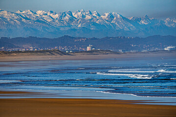Lush green landscape from a hilltop on a sunny day with a clear blue sky. Snow-capped Picos de...