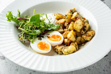  A delicious meal featuring two soft-boiled eggs with runny yolks, seasoned diced potatoes, a fresh salad, and a dollop of creamy dressing, elegantly presented in a white bowl.