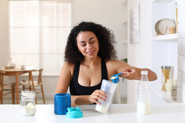 Beautiful woman making protein shake at white table indoors