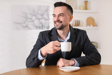 Handsome middle aged man with cup of drink at table indoors