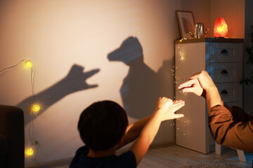 Shadow play. Father with his son making hand gestures like goose and duck on wall at home, closeup