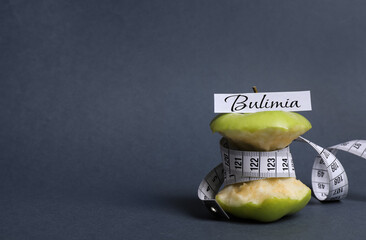 Apple core with measuring tape and word Bulimia on dark grey background, space for text