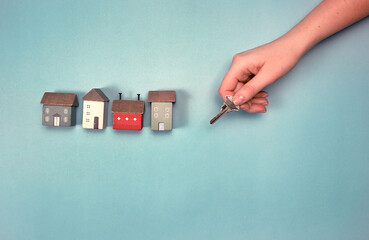 Small houses different colors and a key in a hand with a blue background, home rentals, landlord...