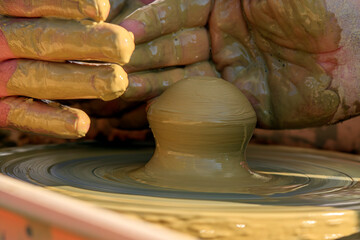 Hands covered in clay gently shape a spinning piece on a pottery wheel, capturing the moment of artistic creation. The earthy tones of the clay contrast with the focused energy of the potter's hands.