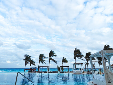 View of swimming pool and tropical beach with palm trees at overcast weather