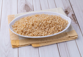 Cooked brown whole rice in a plate over wooden table
