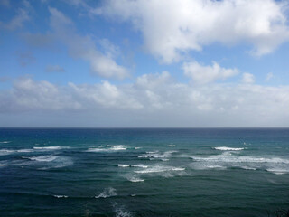 Vibrant waves roll on the shores of Oahu, Hawaii under a bright blue sky with scattered clouds in the afternoon