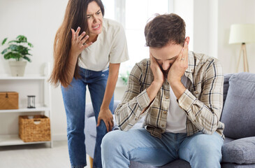 Family couple is having a quarrel at home, with the wife angrily shouting at depressed husband, who is suffering from a headache. The scene shows conflict, stress, and emotional abuse.