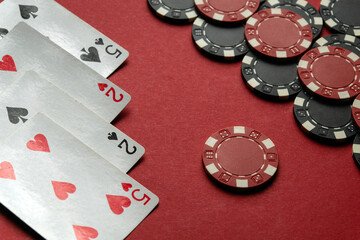 Four playing cards depicting a pair of twos and a pair of fives lie next to a stack of red and black chips on a bright red table, creating an inviting atmosphere for poker lovers