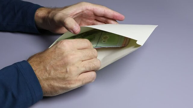 Close up view of man's hands, envelope and Thai baht (THB) cash money banknotes. Concept of corruption, tax cheating, illegal income, financial fraud, bribe, unofficial salary in Thailand.