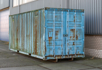 steel blue shipping container stands outside on the street next to a factory building