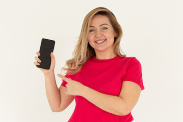 Fototapeta premium Close up portrait of a smiling woman showing blank screen mobile phone while standing isolated over white background
