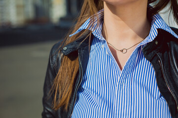 A woman showcases trendy jewelry while wearing a striped blouse and a leather jacket, standing in...