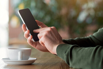 Cropped of man using smartphone at cafe, drinking coffee, side view