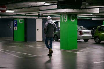A man in a hoodie walks through an empty parking lot © Sergey