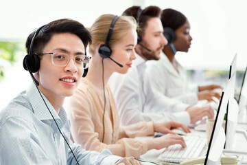 Asian call centre manager smiling and looking at camera in light office, space for text. Helpdesk...