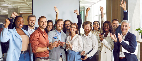 Portrait of diverse happy business people standing in office applauding and looking cheerful at the camera. Group of coworkers men and women smiling indoors. Team work concept. Banner.