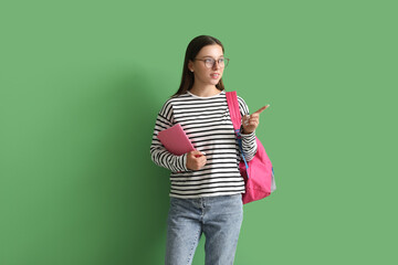 Happy female student with backpack and notebook pointing at something on green background