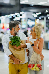 Happy senior couple holding grocery bags in supermarket