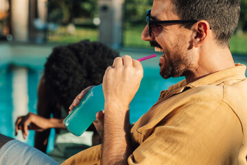 Man enjoying a refreshing drink by the pool on a summer day