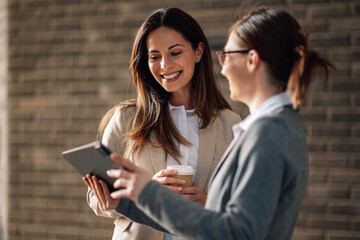 Two businesswomen sharing a digital tablet and a coffee break