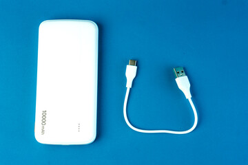 A white 10000mAh power bank with a USB charging cable on a blue background. Ideal for fast charging smartphones, tablets, and electronic devices. Portable and compact for travel use.