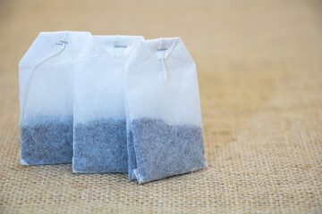 A set of three white tea bags with gray tea inside, placed on burlap fabric. The tea bags have...