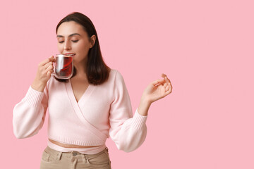 Beautiful young woman with glass cup of hot mulled wine on pink background