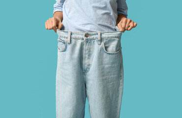 Beautiful young Asian woman in loose jeans on blue background, closeup