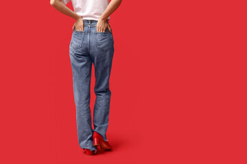 Naklejka premium Woman in blue jeans and red shoes, back view on red background