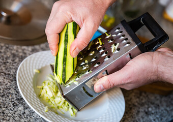 Hands rubs zucchini vegetable on grater close-up